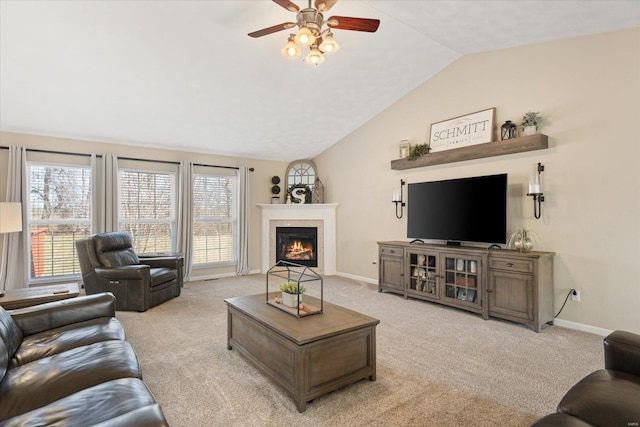 living area with baseboards, vaulted ceiling, a glass covered fireplace, and light colored carpet