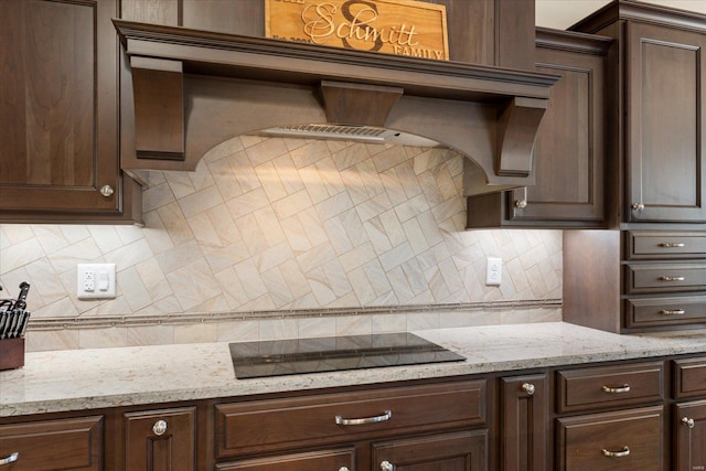 kitchen featuring light stone counters, decorative backsplash, black electric cooktop, and dark brown cabinetry