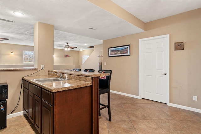 kitchen with ceiling fan, a kitchen bar, visible vents, and a sink