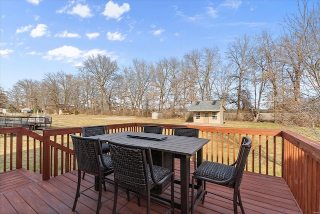 wooden terrace with a yard, outdoor dining area, and an outdoor structure