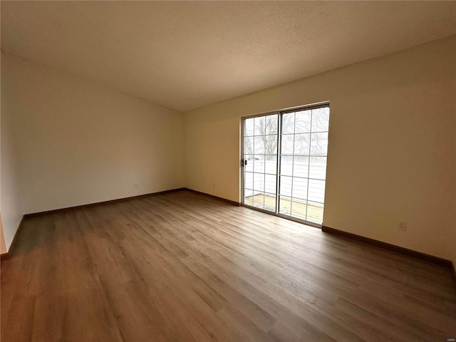 spare room featuring a textured ceiling, baseboards, and wood finished floors