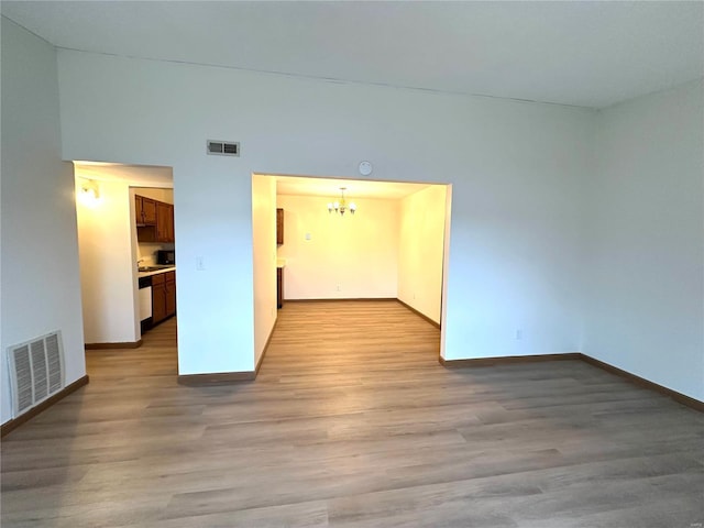 unfurnished room featuring a chandelier, wood finished floors, visible vents, and baseboards