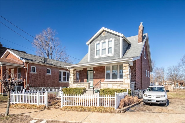 view of front facade featuring a porch, brick siding, a chimney, and a fenced front yard