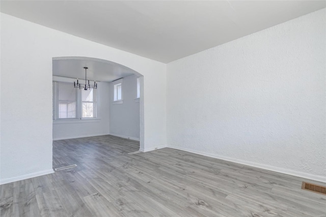 unfurnished room with arched walkways, a chandelier, wood finished floors, visible vents, and baseboards