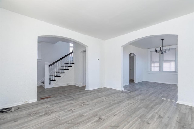 unfurnished room with arched walkways, stairway, wood finished floors, a chandelier, and baseboards