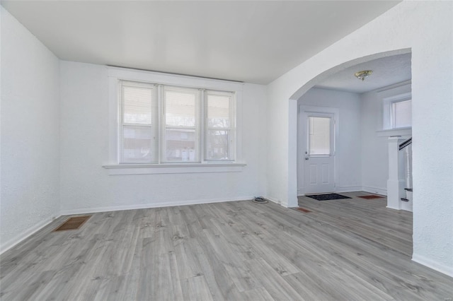 empty room with arched walkways, visible vents, wood finished floors, and a wealth of natural light