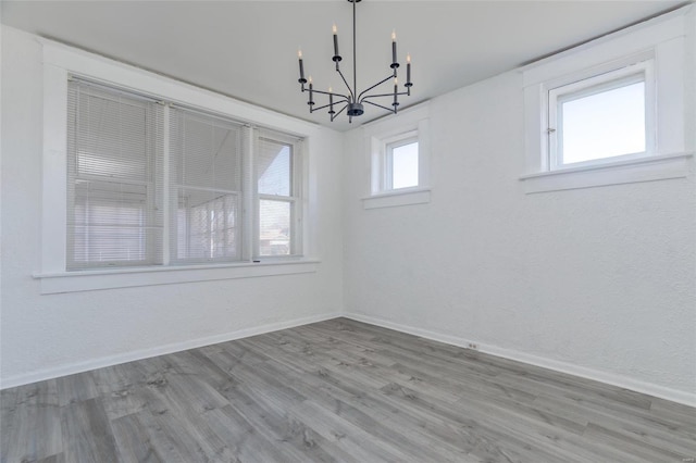 empty room with a chandelier, wood finished floors, and baseboards