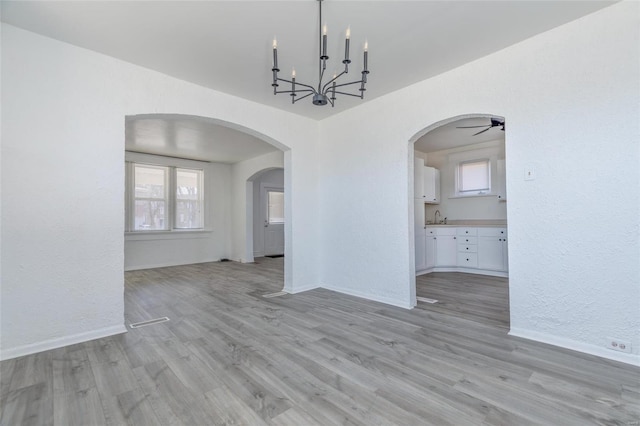 unfurnished dining area featuring a chandelier, arched walkways, a sink, baseboards, and light wood finished floors