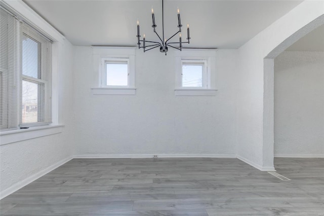 unfurnished dining area featuring a chandelier, baseboards, and wood finished floors