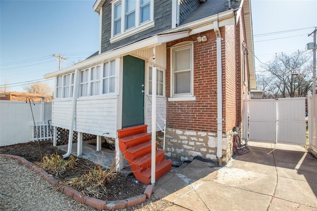 entrance to property with roof with shingles, a gate, fence, and brick siding