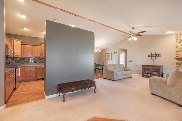 living area with baseboards, light colored carpet, vaulted ceiling, a stone fireplace, and ceiling fan with notable chandelier