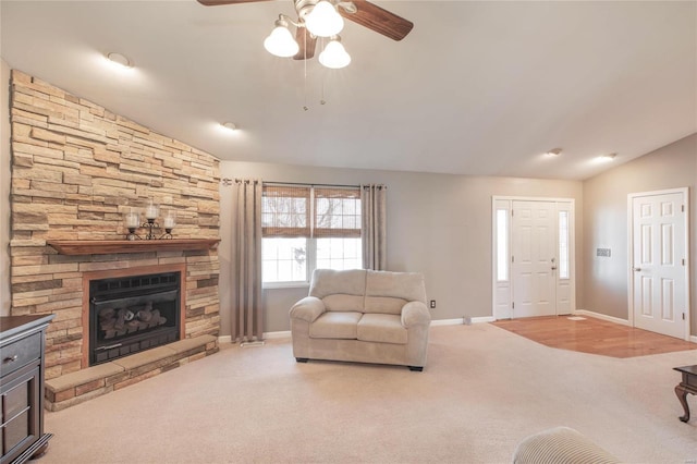 living area featuring lofted ceiling, carpet flooring, ceiling fan, a stone fireplace, and baseboards