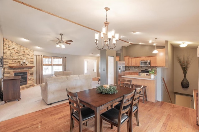 dining area featuring light wood-type flooring, ceiling fan, vaulted ceiling, and a stone fireplace