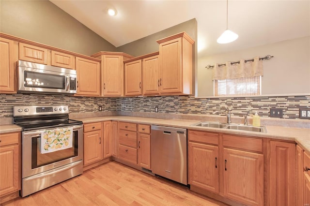 kitchen featuring light wood finished floors, lofted ceiling, stainless steel appliances, light brown cabinetry, and a sink