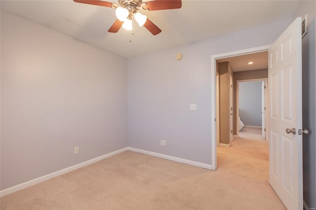 spare room with a ceiling fan, light carpet, and baseboards