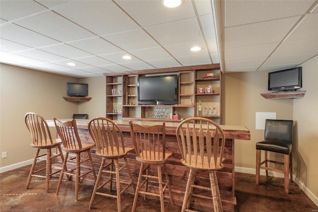 bar featuring a dry bar, recessed lighting, a drop ceiling, concrete floors, and baseboards