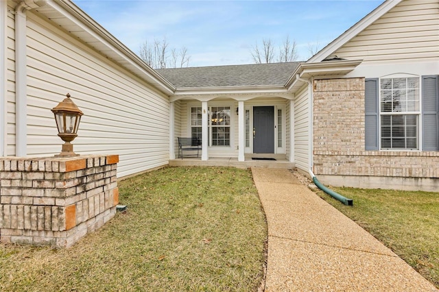 view of exterior entry with covered porch, brick siding, a lawn, and a shingled roof