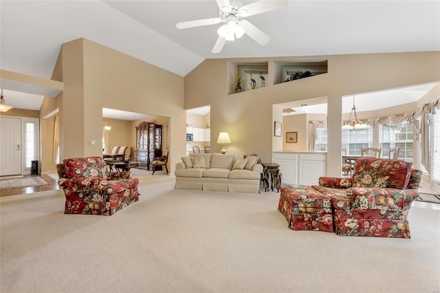 carpeted living area with high vaulted ceiling and ceiling fan with notable chandelier