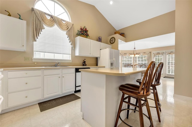 kitchen featuring dishwashing machine, a breakfast bar, a sink, light countertops, and white fridge with ice dispenser