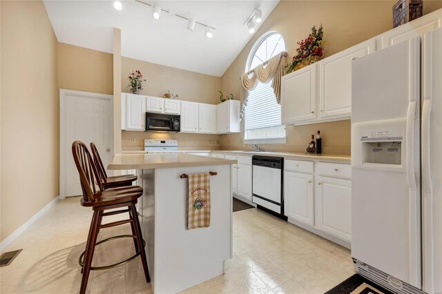 kitchen with white appliances, a kitchen breakfast bar, vaulted ceiling, light countertops, and white cabinets