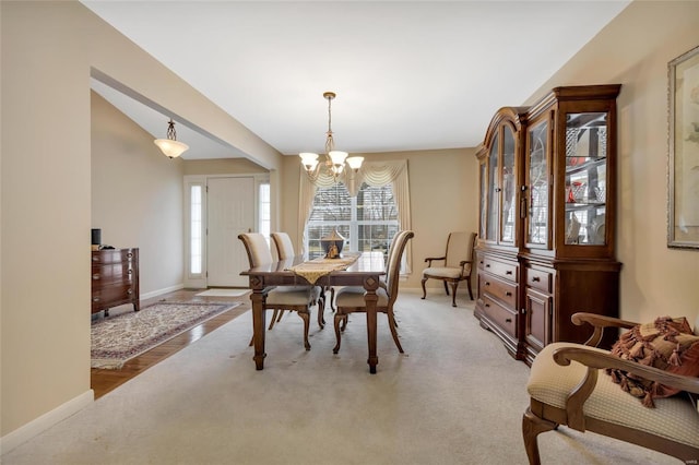 dining room featuring light colored carpet, a notable chandelier, and baseboards