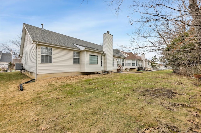 rear view of property featuring a chimney, a lawn, and roof with shingles