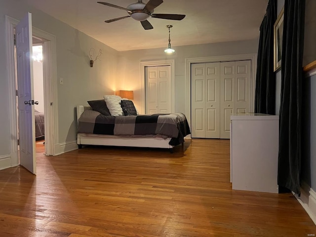 bedroom with light wood-type flooring, ceiling fan, baseboards, and two closets