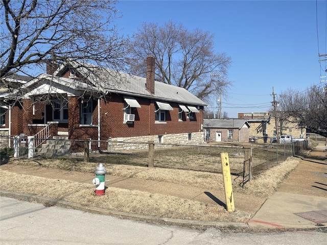 view of front facade featuring brick siding, a fenced front yard, and a chimney