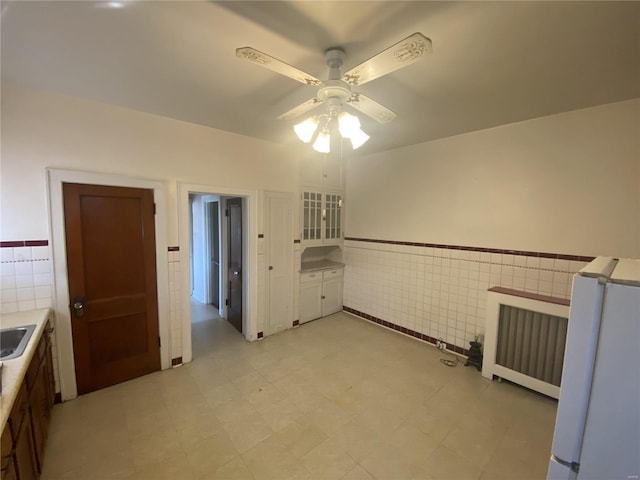 interior space with ceiling fan, light floors, wainscoting, and tile walls