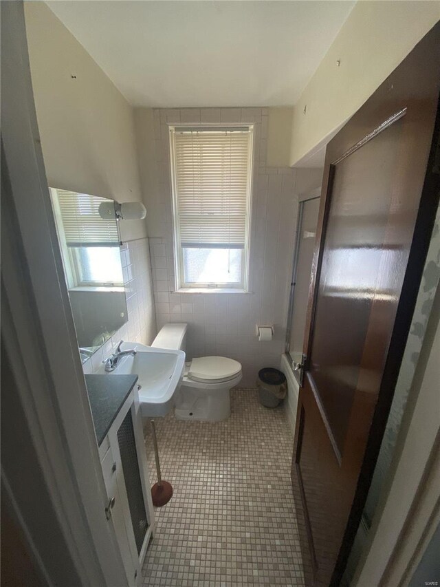 full bathroom with toilet, tile patterned flooring, an enclosed shower, vanity, and tile walls