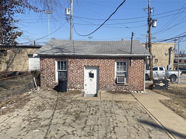 rear view of house with brick siding, roof with shingles, cooling unit, and fence