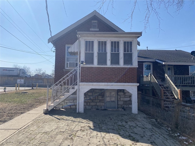 view of front facade featuring brick siding, stairway, and fence