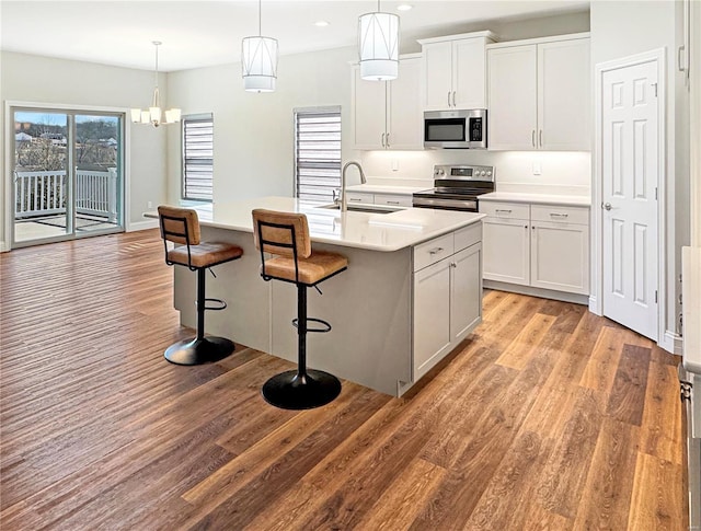 kitchen with light wood-style flooring, appliances with stainless steel finishes, a breakfast bar, light countertops, and a sink