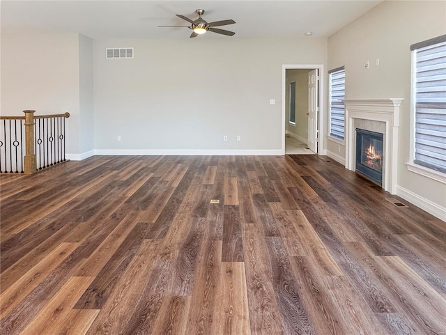 unfurnished living room featuring baseboards, visible vents, dark wood finished floors, and a glass covered fireplace