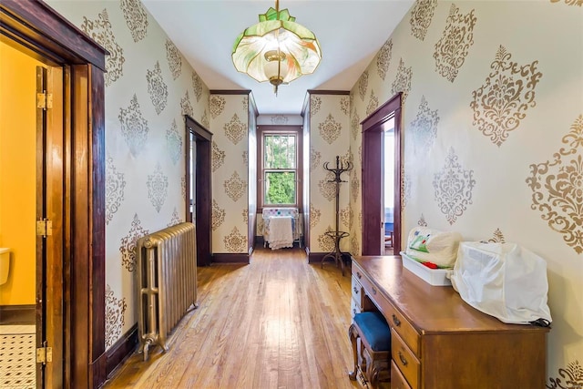 hall with light wood-type flooring, baseboards, radiator heating unit, and wallpapered walls