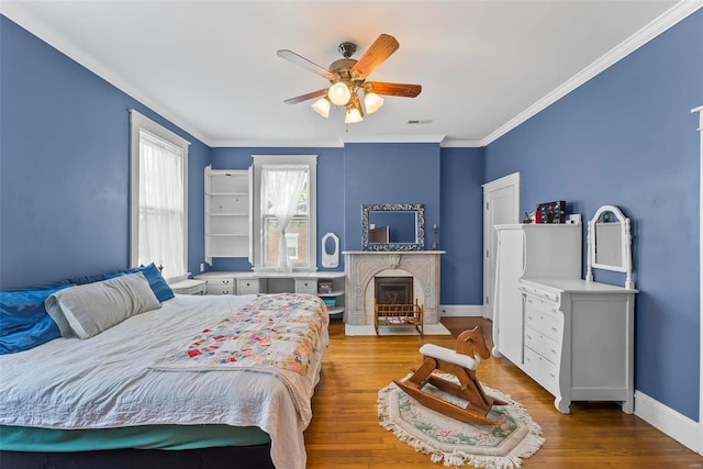 bedroom featuring visible vents, ornamental molding, a glass covered fireplace, wood finished floors, and baseboards