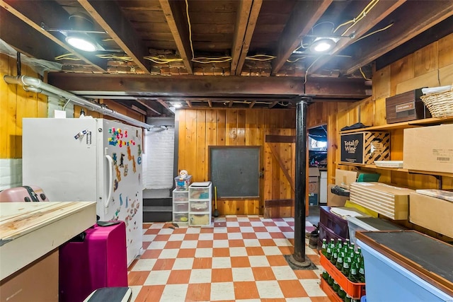 unfinished below grade area with wood walls, freestanding refrigerator, and tile patterned floors