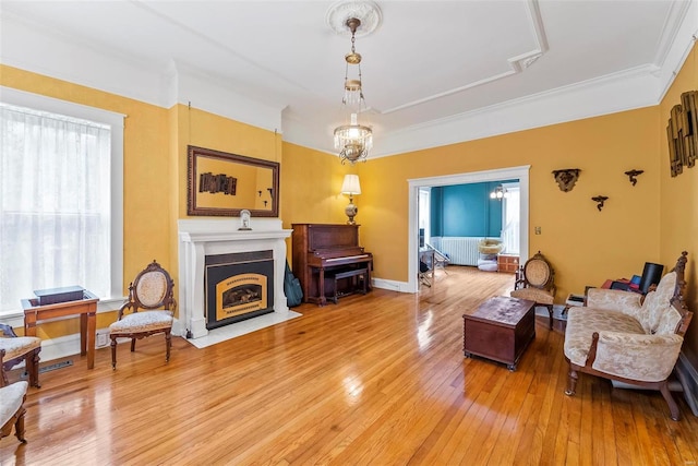 living room with baseboards, a fireplace with flush hearth, ornamental molding, light wood-style floors, and a notable chandelier