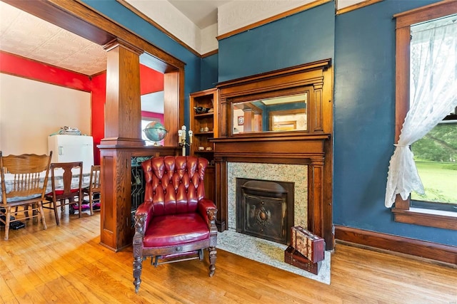 sitting room with a fireplace with flush hearth, wood finished floors, and ornate columns