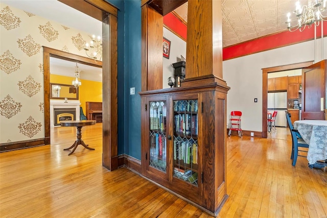 corridor featuring an ornate ceiling, light wood-style floors, a notable chandelier, and baseboards