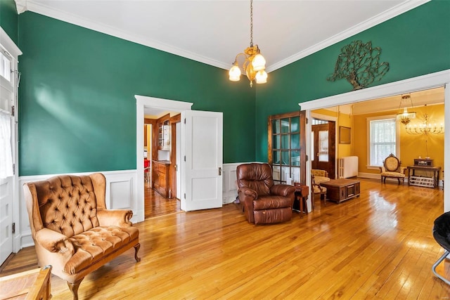 sitting room featuring light wood finished floors, a wainscoted wall, radiator heating unit, ornamental molding, and a chandelier