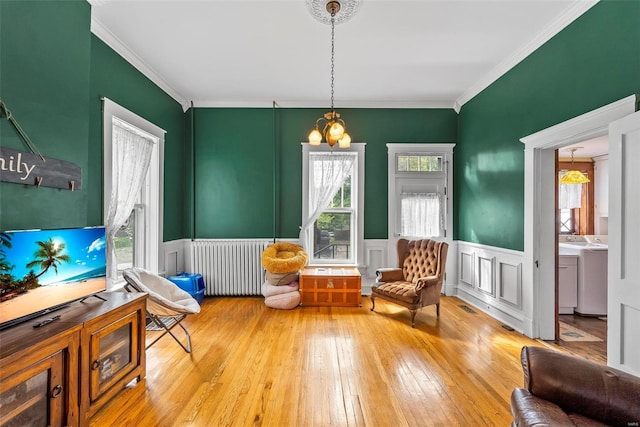 sitting room featuring hardwood / wood-style flooring, a wainscoted wall, ornamental molding, washer / clothes dryer, and radiator heating unit