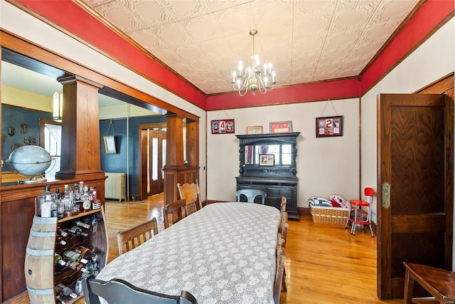 dining area featuring decorative columns, an ornate ceiling, radiator heating unit, wood finished floors, and a chandelier