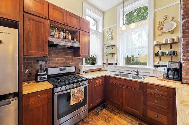 kitchen featuring butcher block countertops, stainless steel appliances, under cabinet range hood, open shelves, and a sink