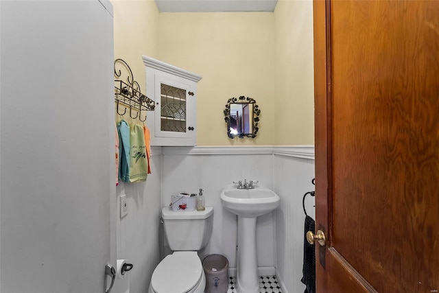 half bathroom with wainscoting, a sink, and toilet