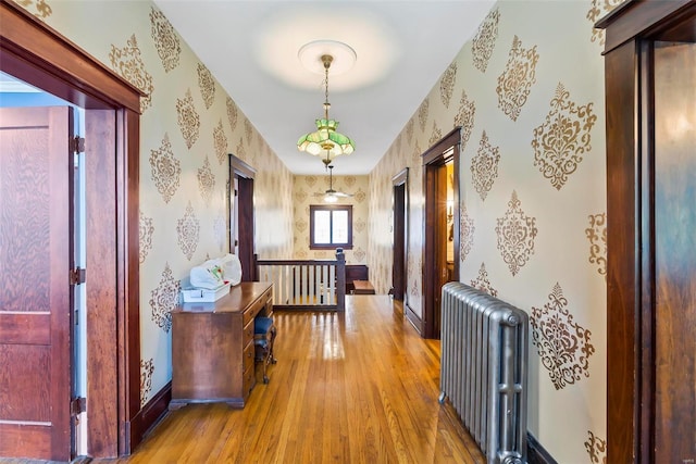 hallway featuring radiator, an upstairs landing, wood finished floors, baseboards, and wallpapered walls