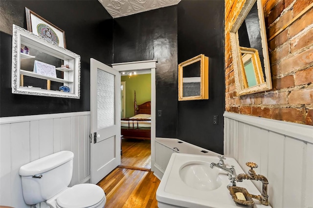 bathroom with toilet, a wainscoted wall, a sink, and wood finished floors