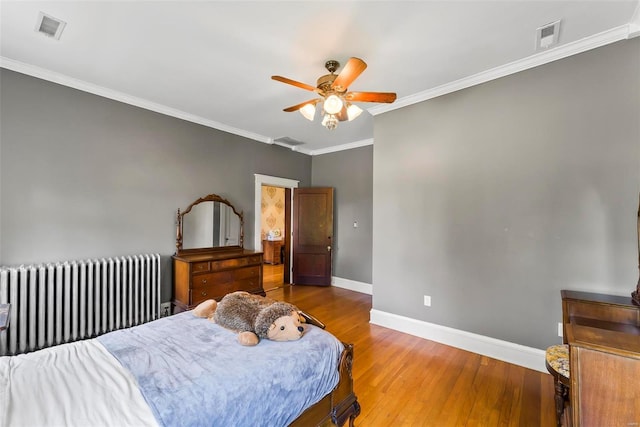 bedroom with crown molding, radiator, visible vents, wood finished floors, and baseboards