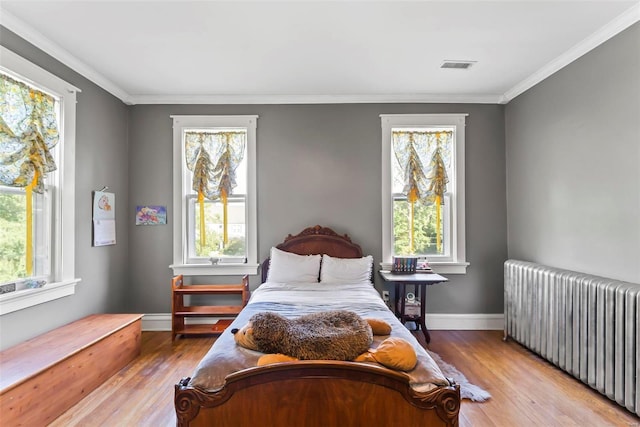 bedroom with multiple windows, radiator heating unit, wood finished floors, and visible vents