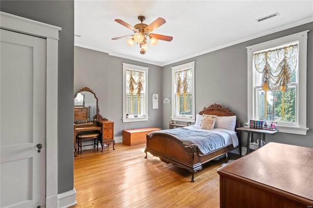 bedroom featuring ceiling fan, visible vents, baseboards, light wood finished floors, and crown molding